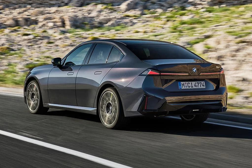 New BMW 320 sedan in dark grey, rear three-quarter view on a coastal road