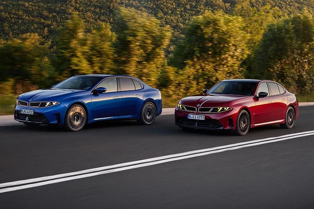 BMW i3 sedan in blue alongside a red BMW 3 Series sedan on a country road