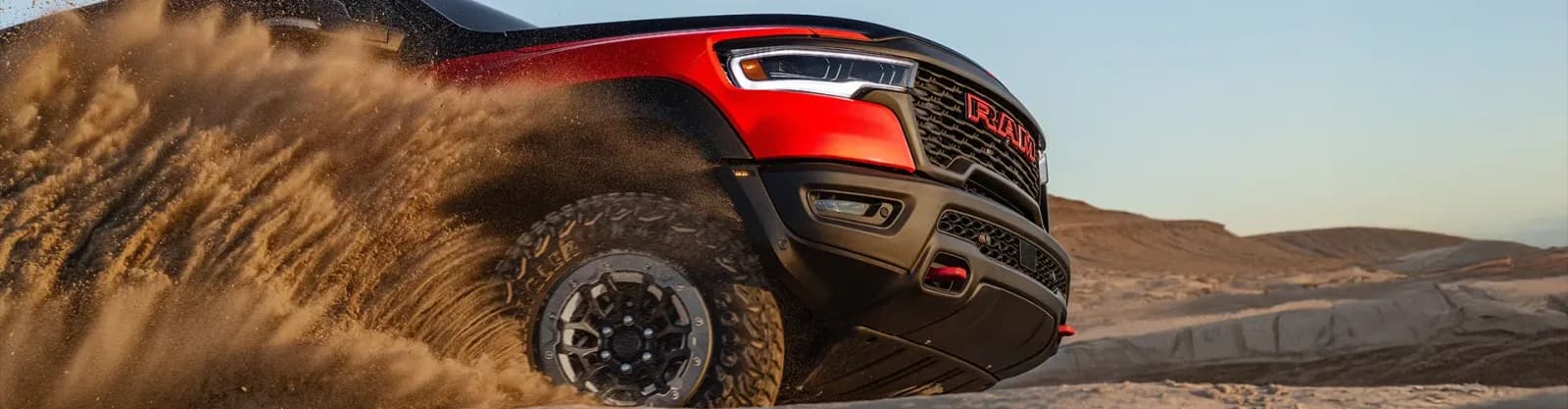 Ram 1500 SRT TRX in red and black, front corner and grille, throwing sand on a desert track