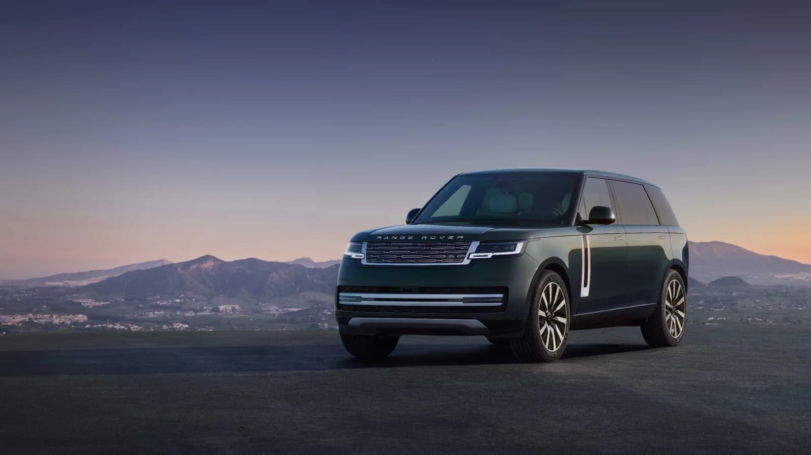 Range Rover Electric in dark green, front three-quarter view on a hilltop at dusk
