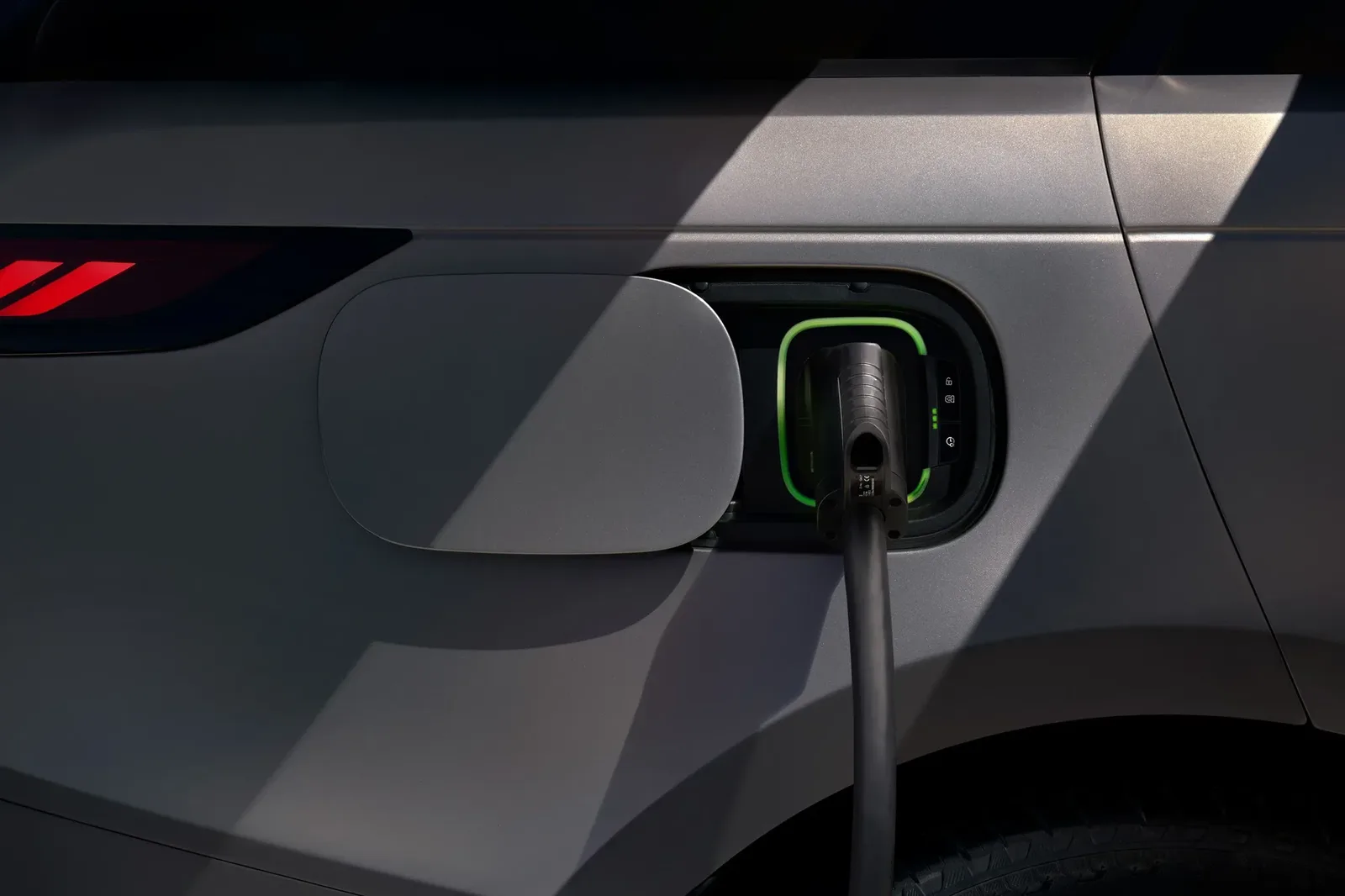Charging cable plugged into the green-lit charge port on the rear flank of a grey Range Rover Sport Electric, with the port flap open
