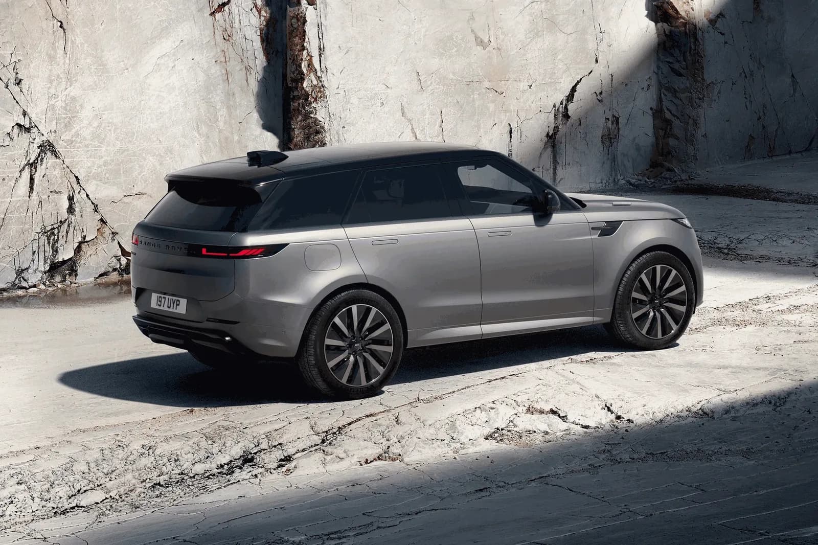 Grey Range Rover Sport Electric with a black roof parked against a marble quarry wall, rear three-quarter view