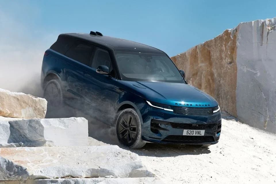 Blue Range Rover Sport Electric with a black roof driving down a dusty track in a white marble quarry, front three-quarter view