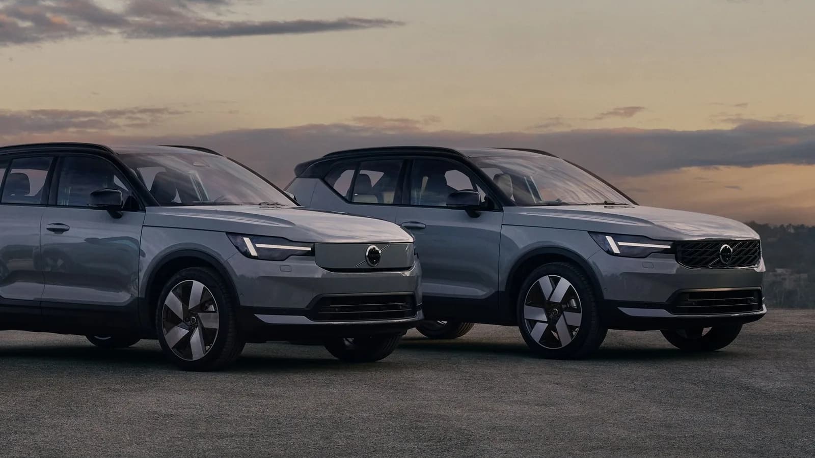 Updated Volvo EX40 (left, with the closed front panel) and XC40 (right, with the grille) in grey, front three-quarter view at dusk