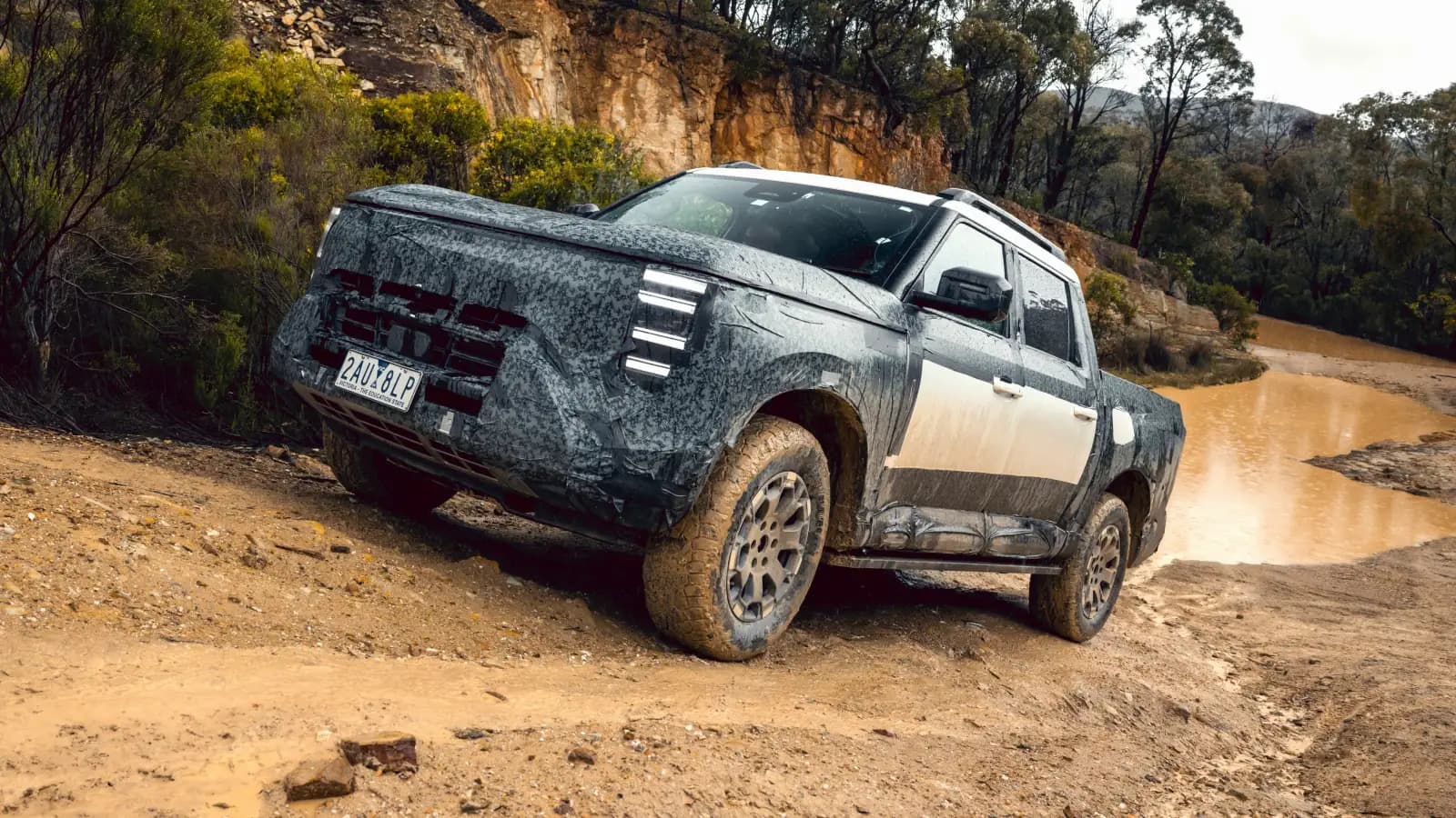 Camouflaged Nissan Navara Pro PHEV prototype on Victorian plates climbing a muddy bush track
