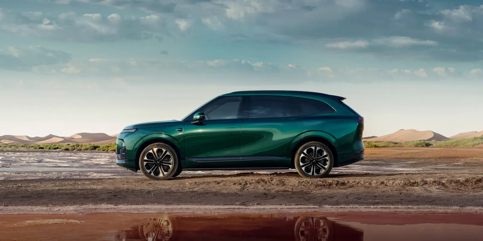 Dark green XPeng G9L large SUV in side profile on a salt flat with sand dunes behind